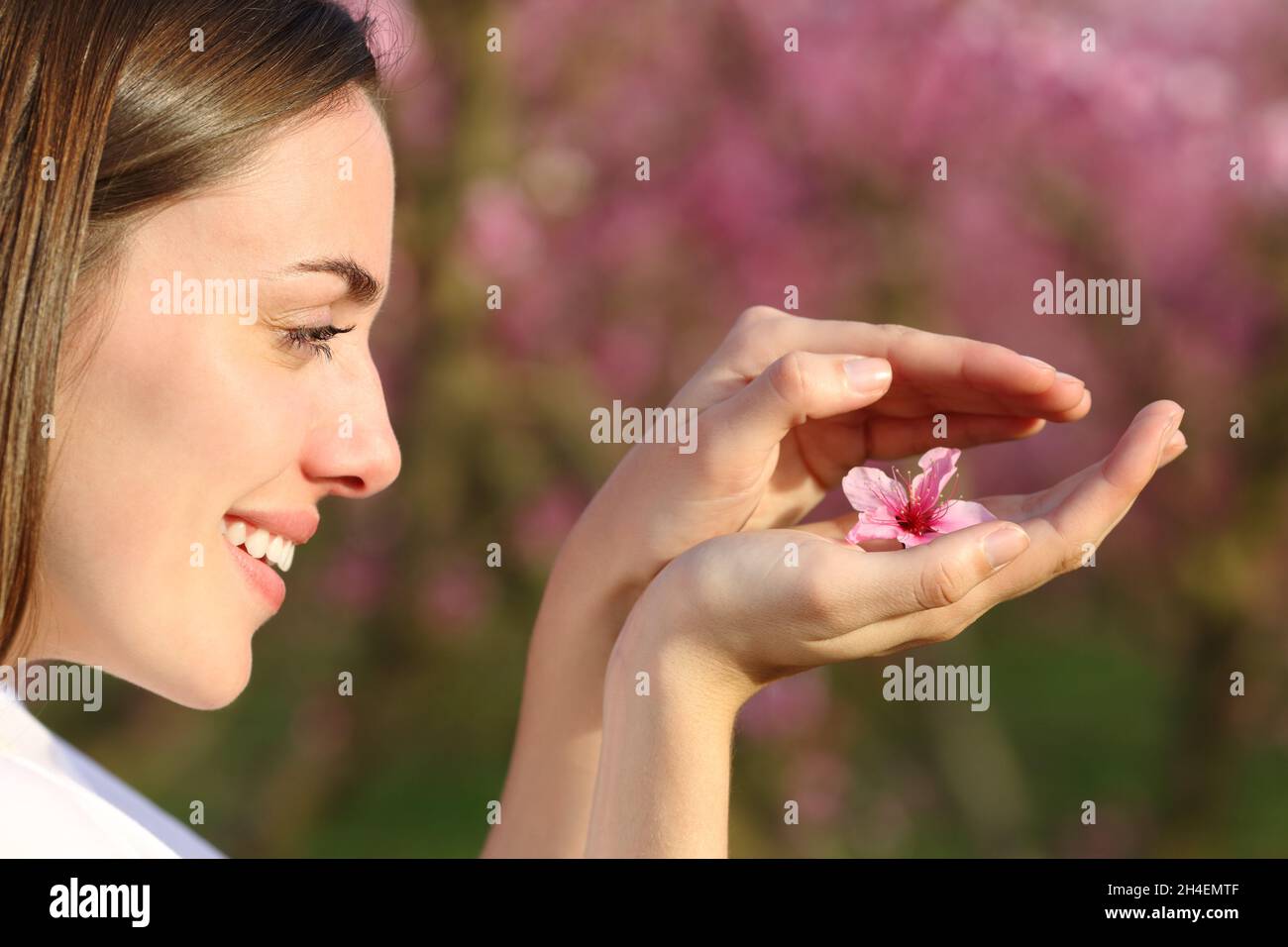 Profil d'une femme heureuse protégeant la fleur dans ses mains dans un champ Banque D'Images