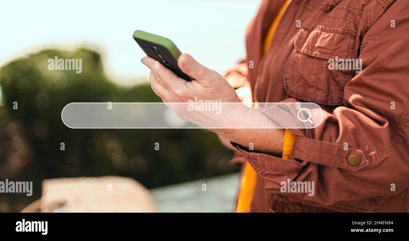 La main de la femme utilise un smartphone pour rechercher des informations sur Internet tout en se tenant dans un parc de la ville Banque D'Images