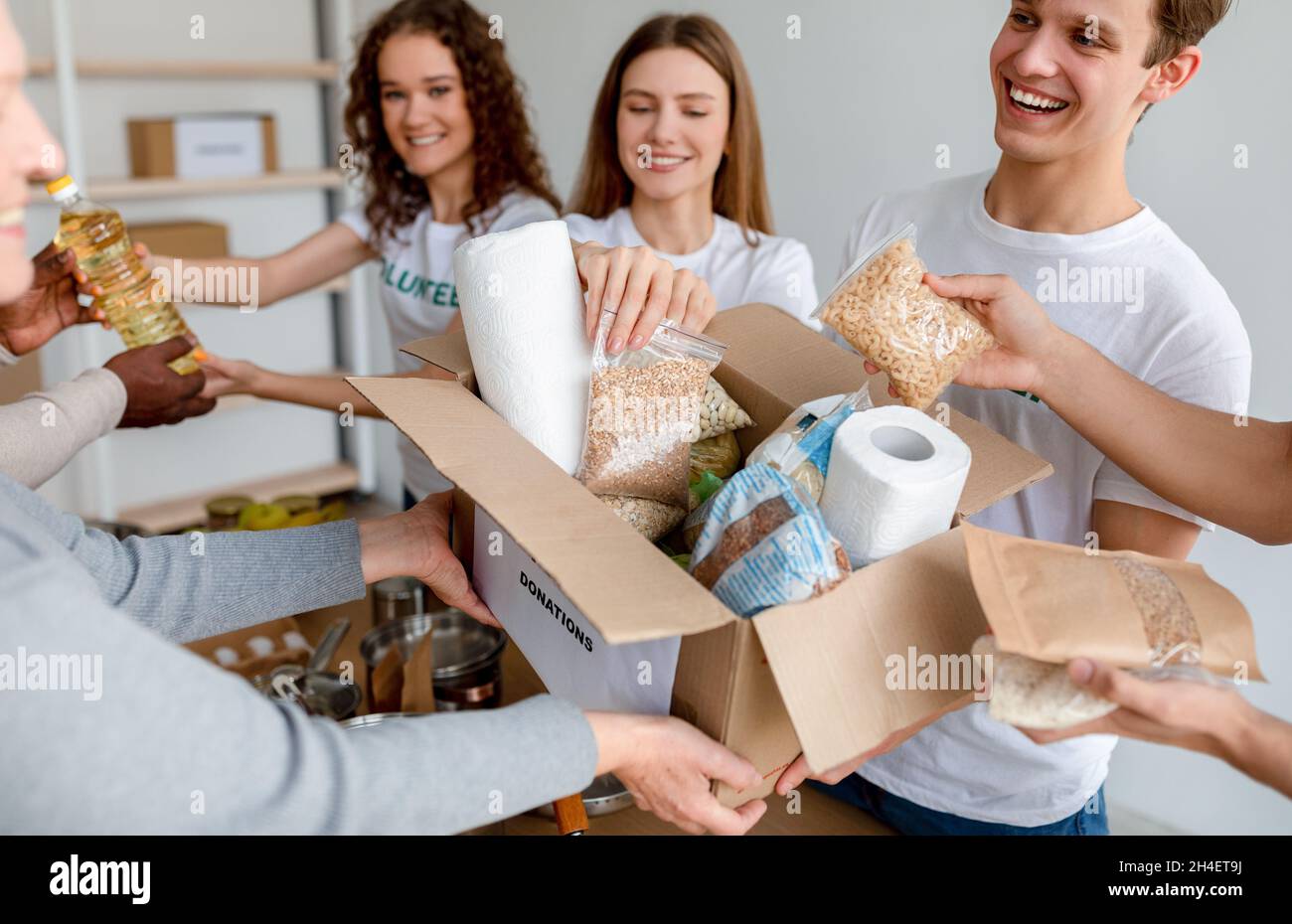 Les jeunes volontaires hommes et femmes emballant les dons de nourriture et de produits d'hygiène personnelle pour les pauvres dans des boîtes en carton Banque D'Images