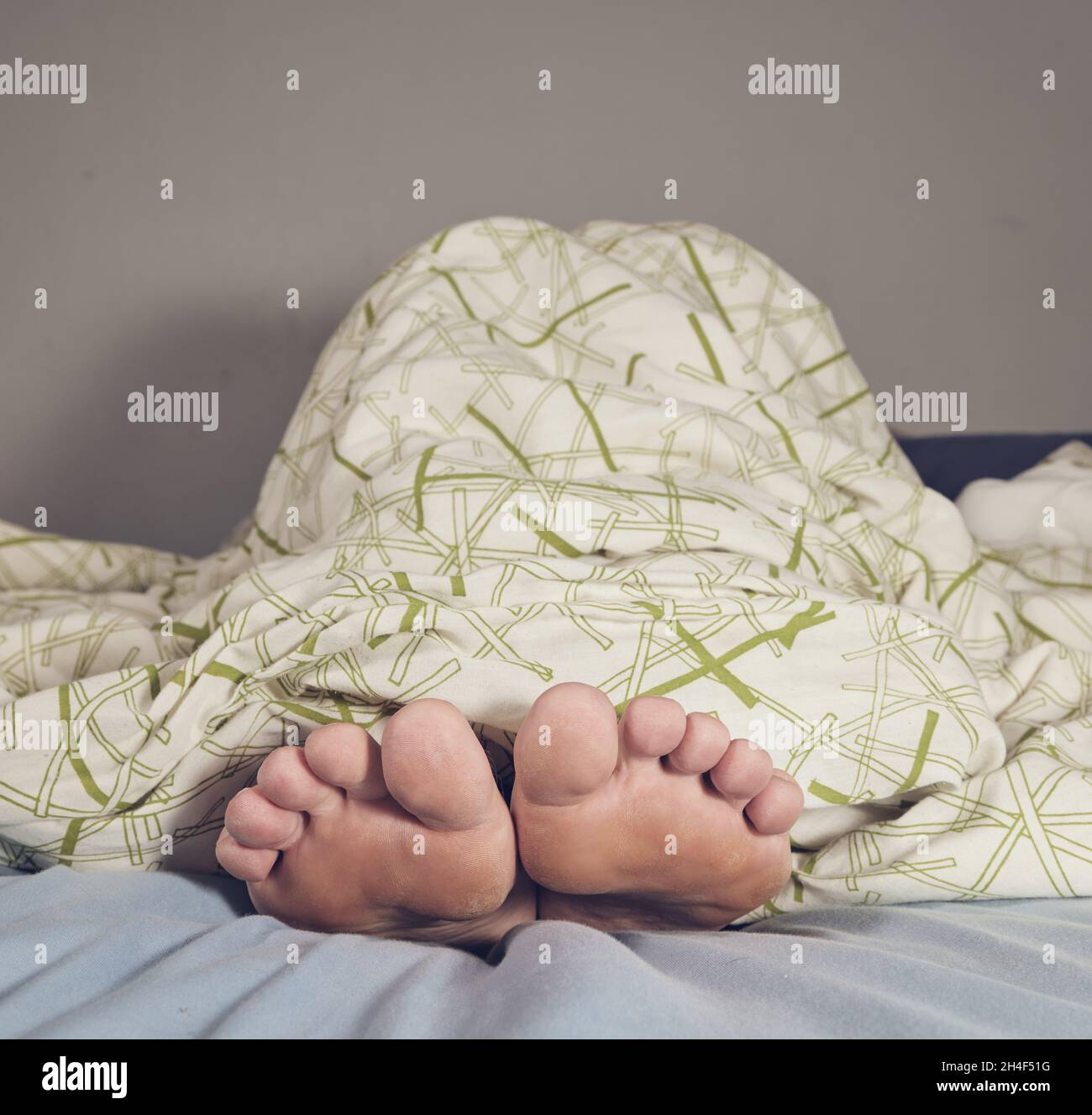 Homme allongé pieds nus dans un lit sous une couverture Banque D'Images