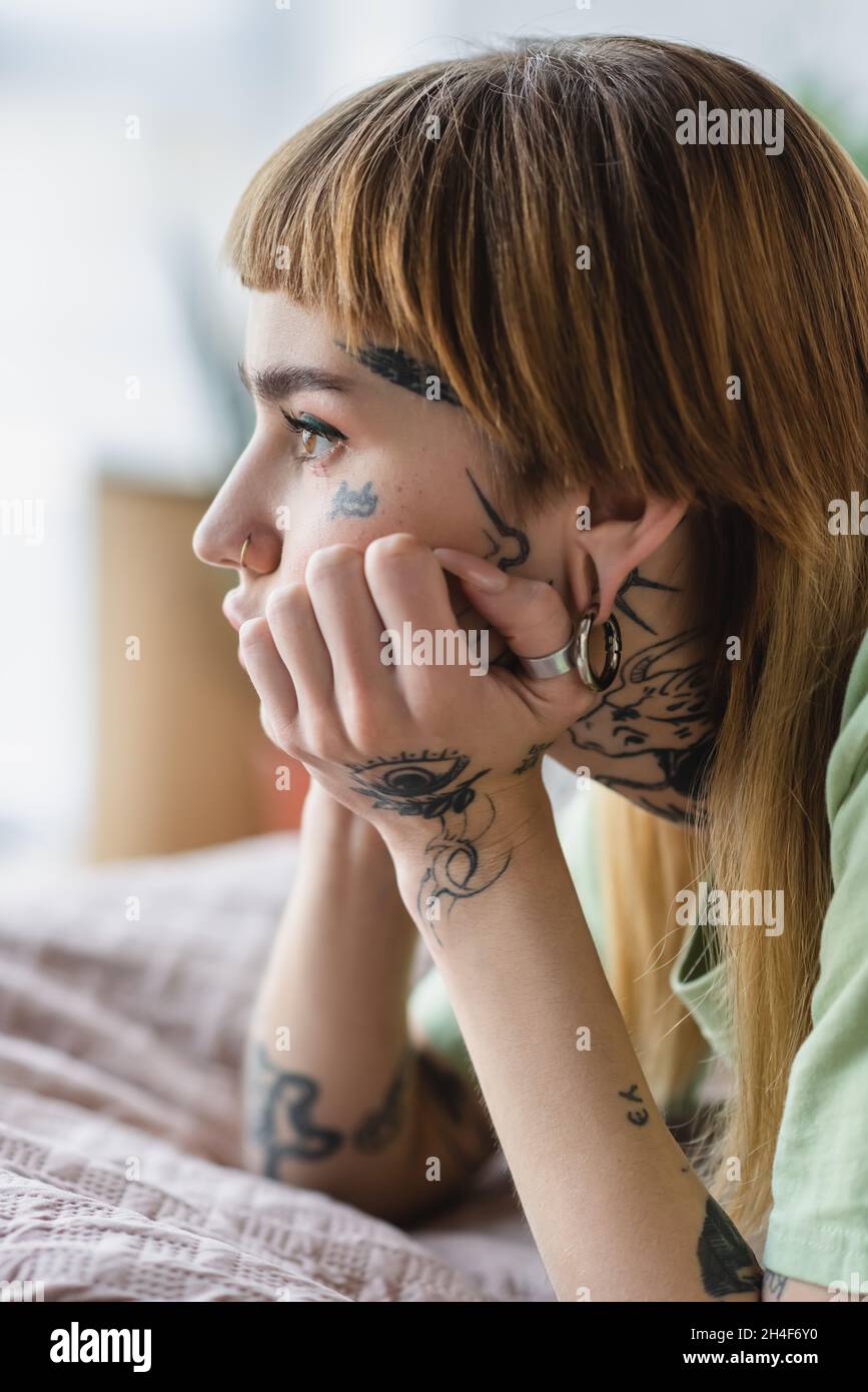 vue latérale de la femme tatouée avec piercing regardant loin sur le lit à la maison Banque D'Images
