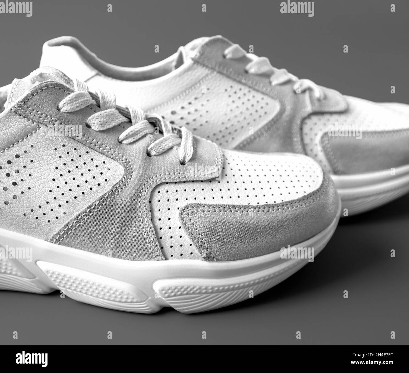 Deux sneakers blanches en cuir pour femme sur fond gris Banque D'Images