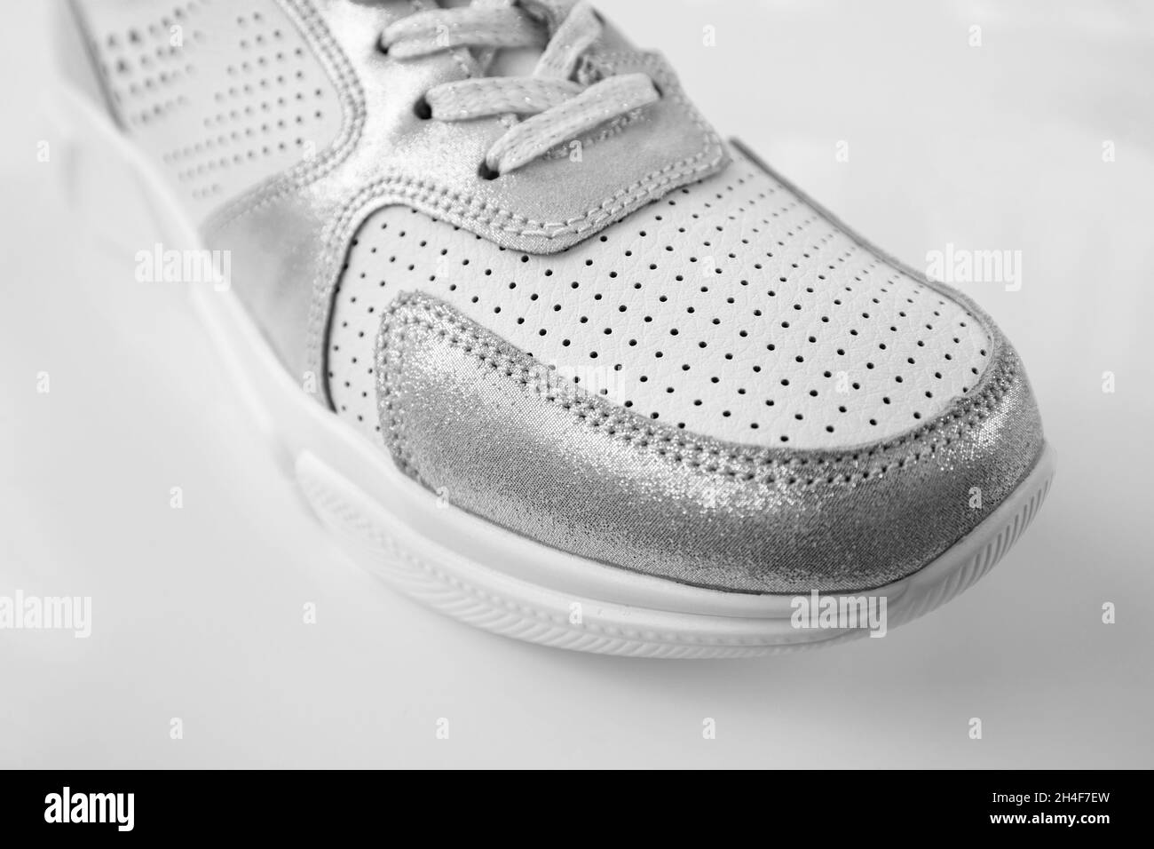 Une sneaker en cuir blanc pour femmes sur fond gris Banque D'Images