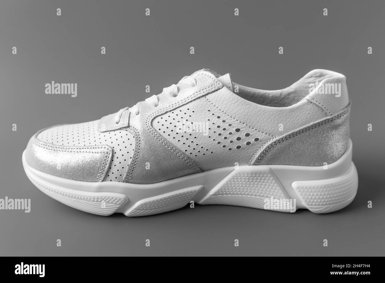 Une sneaker en cuir blanc pour femmes sur fond gris Banque D'Images