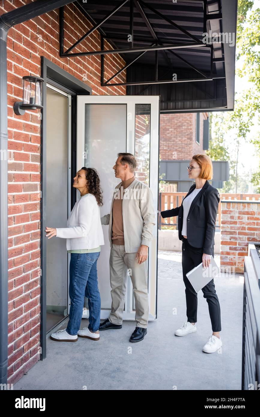 realtor en verre ouvrant la porte tout en couple interracial entrant dans la nouvelle maison Banque D'Images