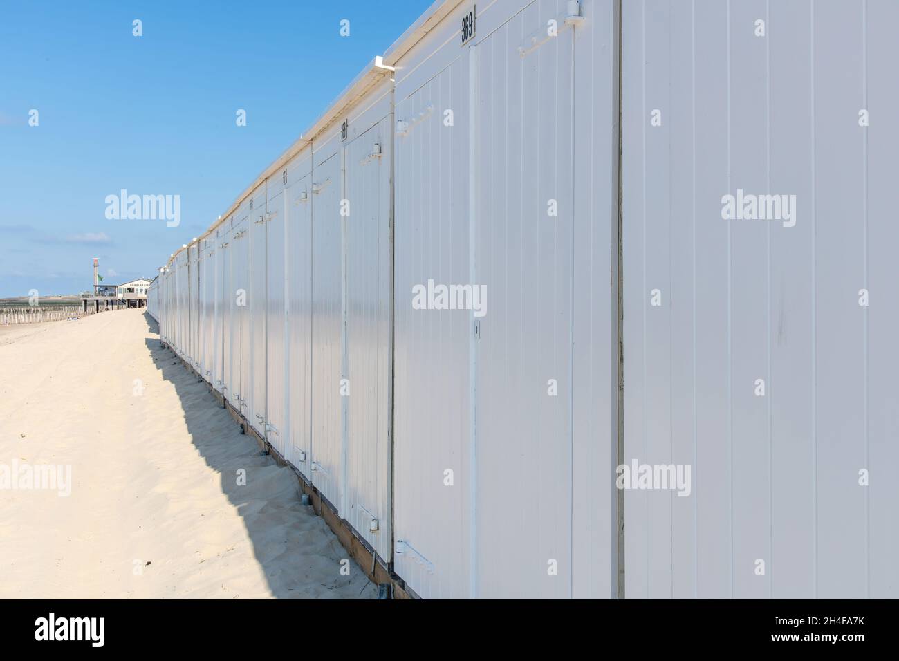 Westkapelle, pays-Bas-mai 2021; vue latérale d'une longue rangée de cabines de plage blanches identiques contre les dunes avec un pavillon de plage dans l'arrière-gro Banque D'Images