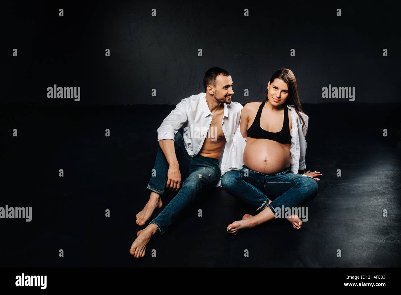 une femme enceinte et un homme dans une chemise blanche et un jean dans un  studio sur fond noir Photo Stock - Alamy