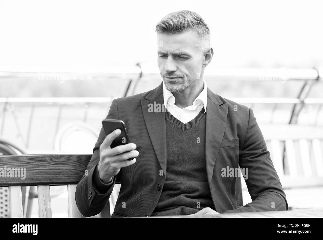 Beau avocat de lire le message d'affaires dans le téléphone mobile assis sur le banc à l'extérieur, sms Banque D'Images