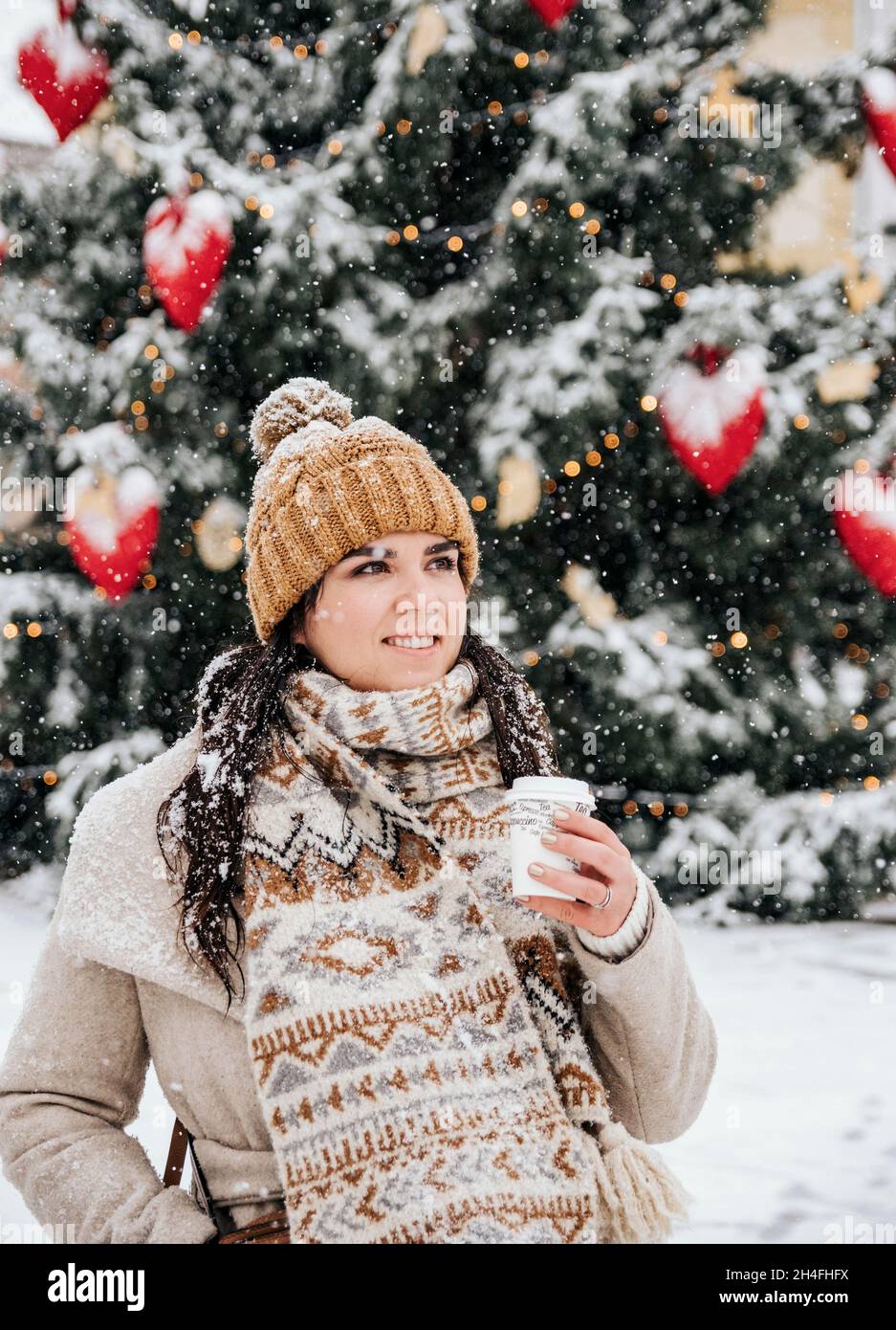 Portrait d'une jeune femme portant des vêtements d'hiver élégants par temps neigeux en ville, buvant du café à emporter Banque D'Images