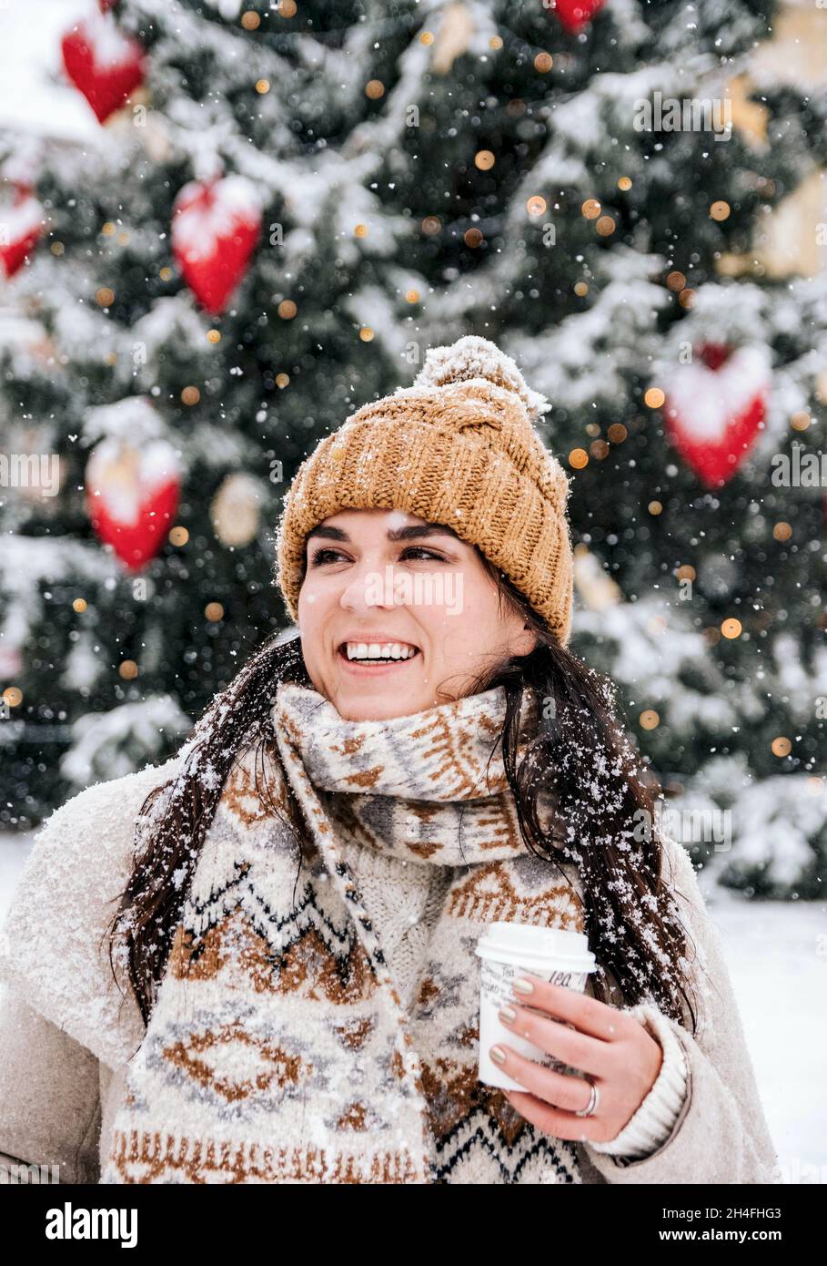 Portrait d'une jeune femme portant des vêtements d'hiver élégants par temps neigeux en ville, buvant du café à emporter Banque D'Images