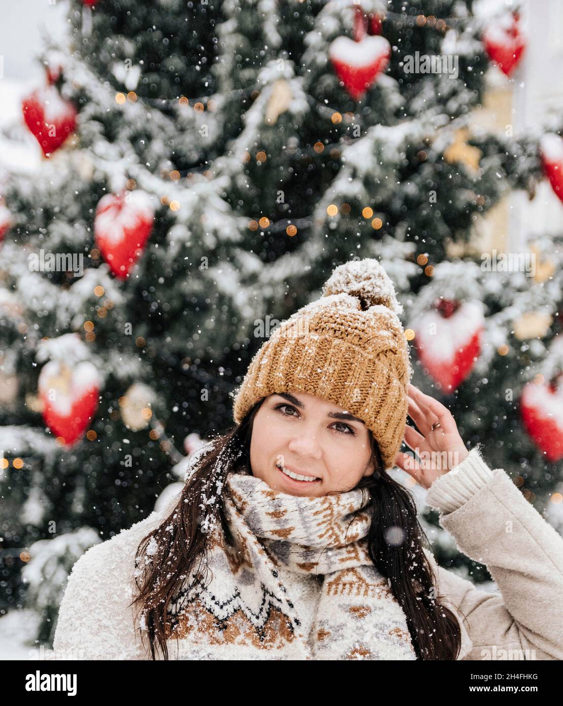 Portrait d'une jeune femme portant des vêtements d'hiver élégants, debout devant l'arbre de noël lors d'une journée enneigée en ville Banque D'Images