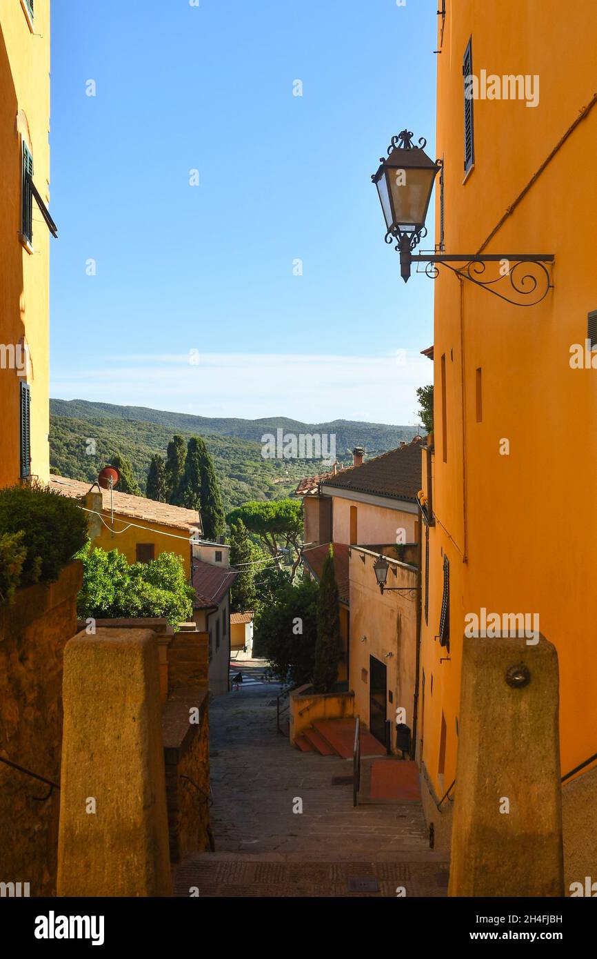 Une montée, ruelle étroite dans le village médiéval avec les collines toscanes en arrière-plan en été, Castagneto Carducci, Livourne, Toscane, Italie Banque D'Images