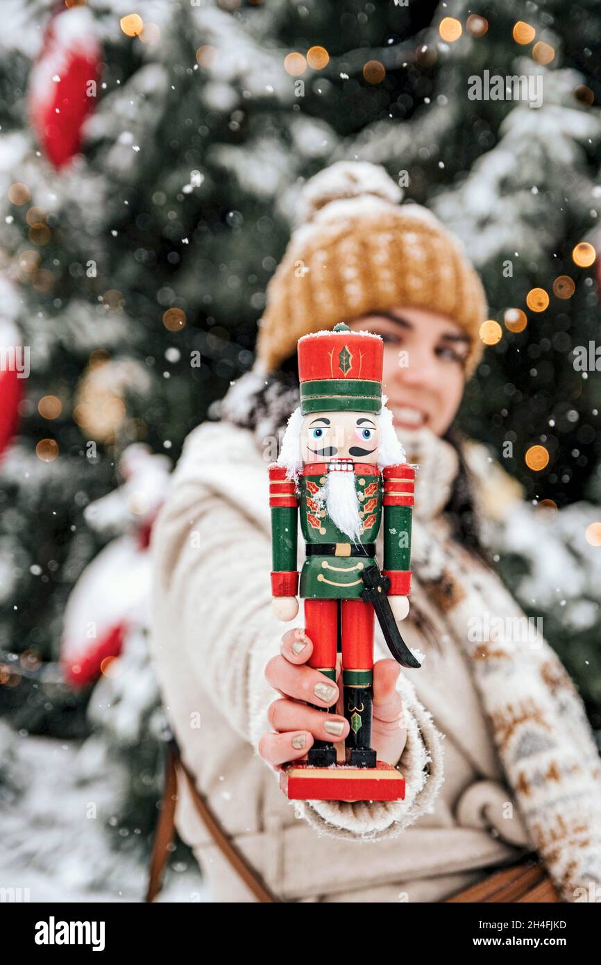 Image sélective de la femme tenant un soldat de casse-noisette vers la caméra lors d'une journée enneigée devant l'arbre de noël en ville Banque D'Images