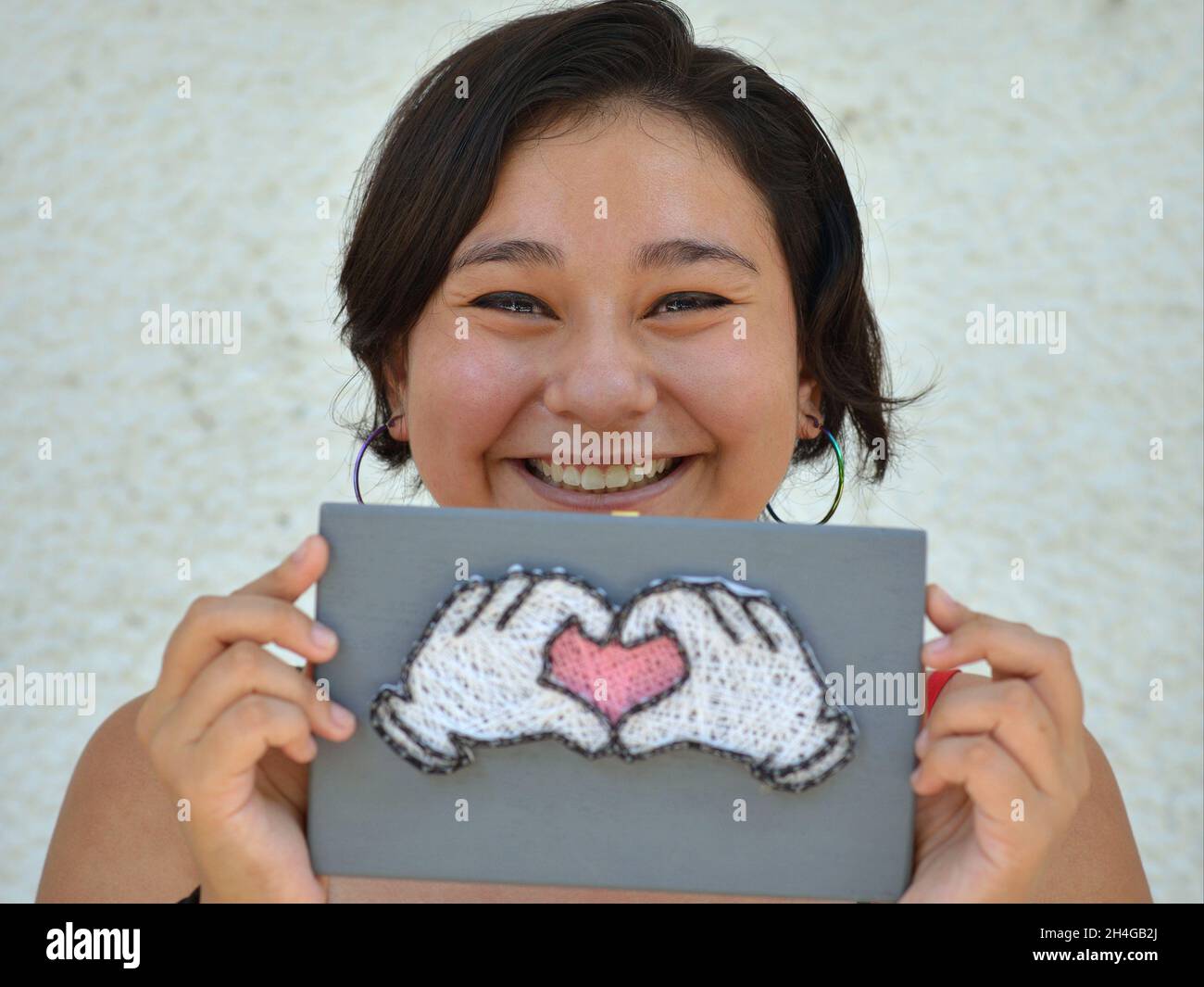 Une jeune femme mexicaine joyeuse et positive sourit au spectateur et tient avec les deux mains un signe avec le symbole de coeur de main. Banque D'Images