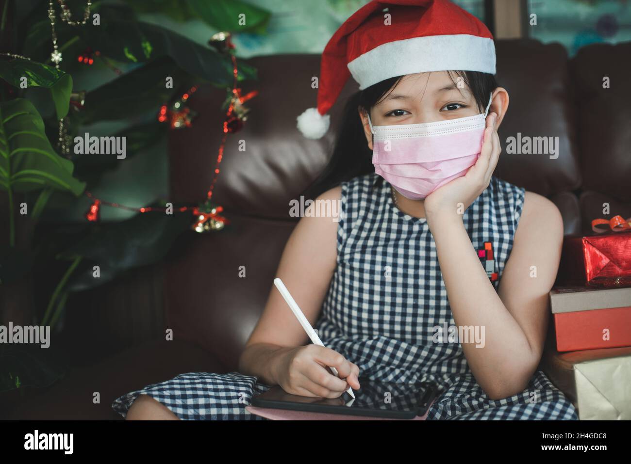 Une fille asiatique pense à de bons voeux à écrire pour les autres.Une fille portant un masque utilise un comprimé pour écrire pendant Noël et le nouvel an Banque D'Images