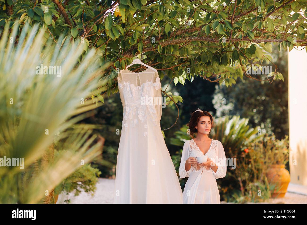 Une belle mariée se tient à côté d'une robe de mariage avec une tasse de  thé dans un ensemble de boudoir à côté d'une villa en Italie.matin de la  mariée en Toscane