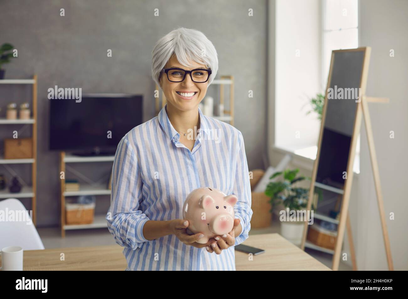 Portrait d'une femme âgée heureuse tenant une banque de porc avec ses économies et sourire Banque D'Images