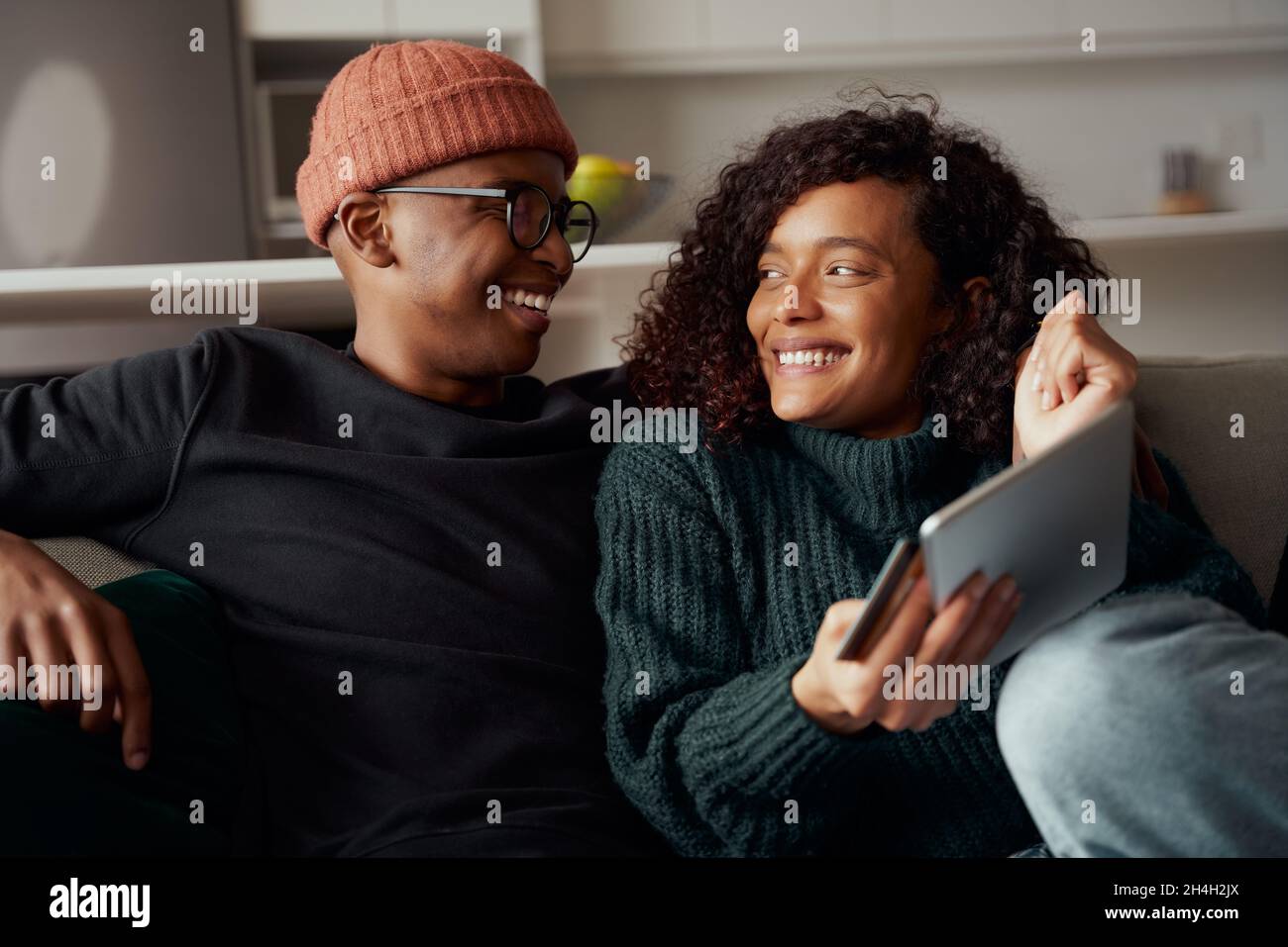 Un couple multiethnique se réjouit de l'achat en ligne effectué à l'aide d'une tablette sur un canapé dans le salon Banque D'Images