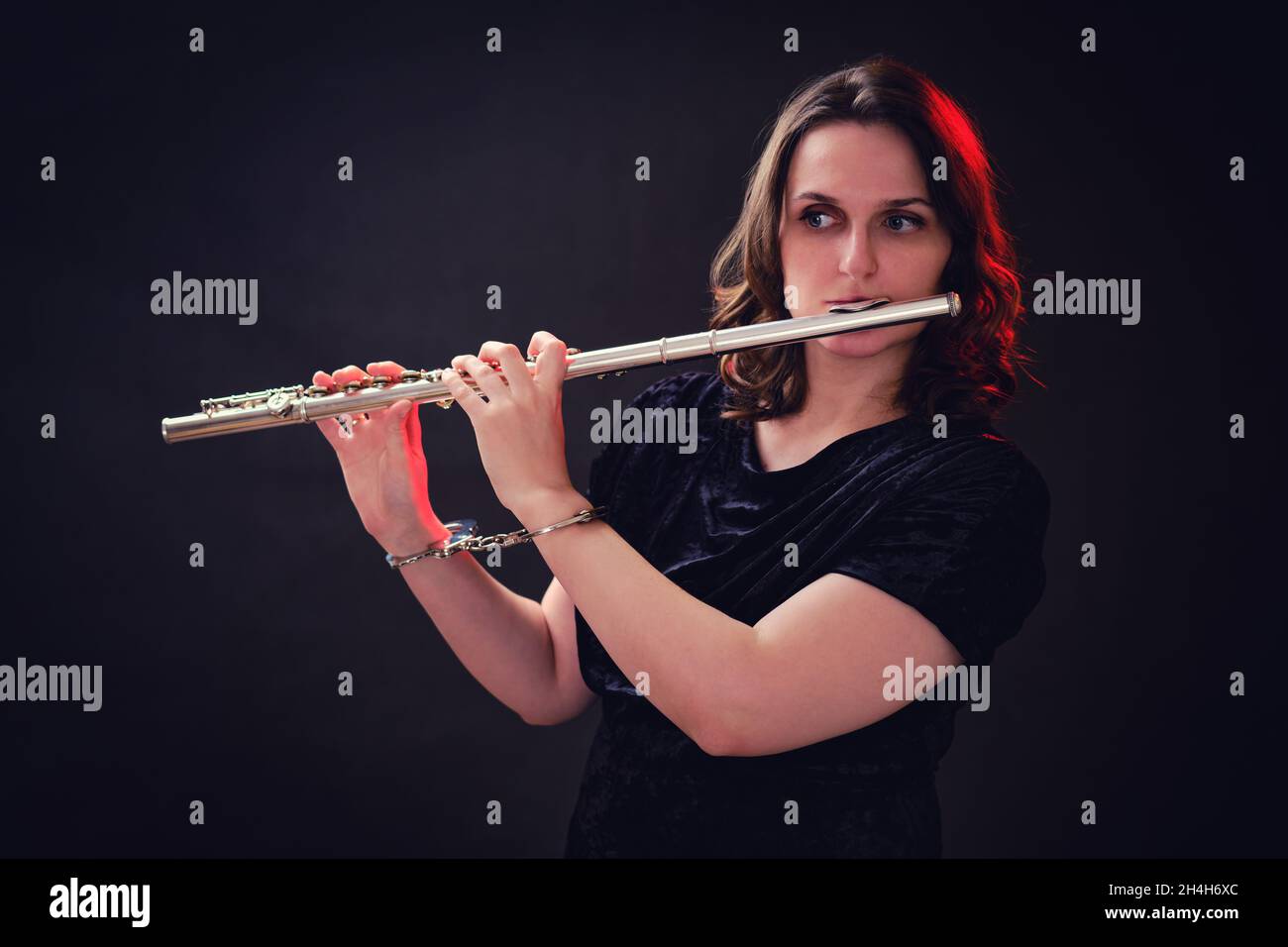 Femme musicienne avec une flûte aux mains menottées sur un fond sombre de studio.Les problèmes de la comédie musicale aux concerts, le concept de non-liberté et a Banque D'Images