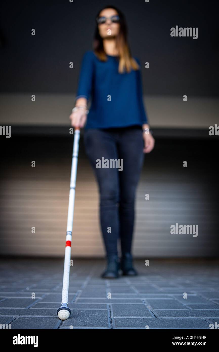 Une jeune femme malvoyante marchant dans les rues de la ville, utilisant sa canne blanche pour mieux naviguer dans l'espace urbain et pour se rendre à destination en toute sécurité Banque D'Images