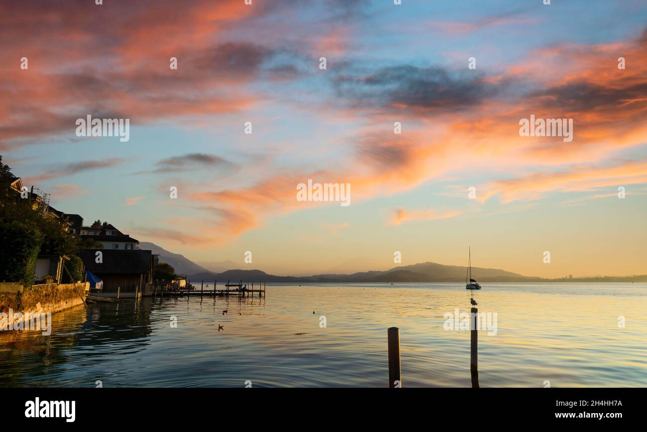 Vue sur le lac Zugersee depuis la ville suisse de Zug, au coucher du soleil et calme avec le ciel nuageux bordé par la lumière du soleil couchant. Banque D'Images