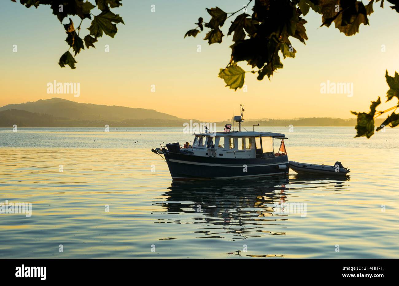 Petit bateau de plaisance sur un lac calme au coucher du soleil, reflétant les tons dorés de la lumière du soleil.Concept de loisirs et de tranquillité. Banque D'Images