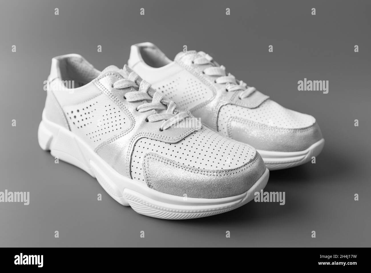 Deux sneakers blanches en cuir pour femme sur fond gris Banque D'Images