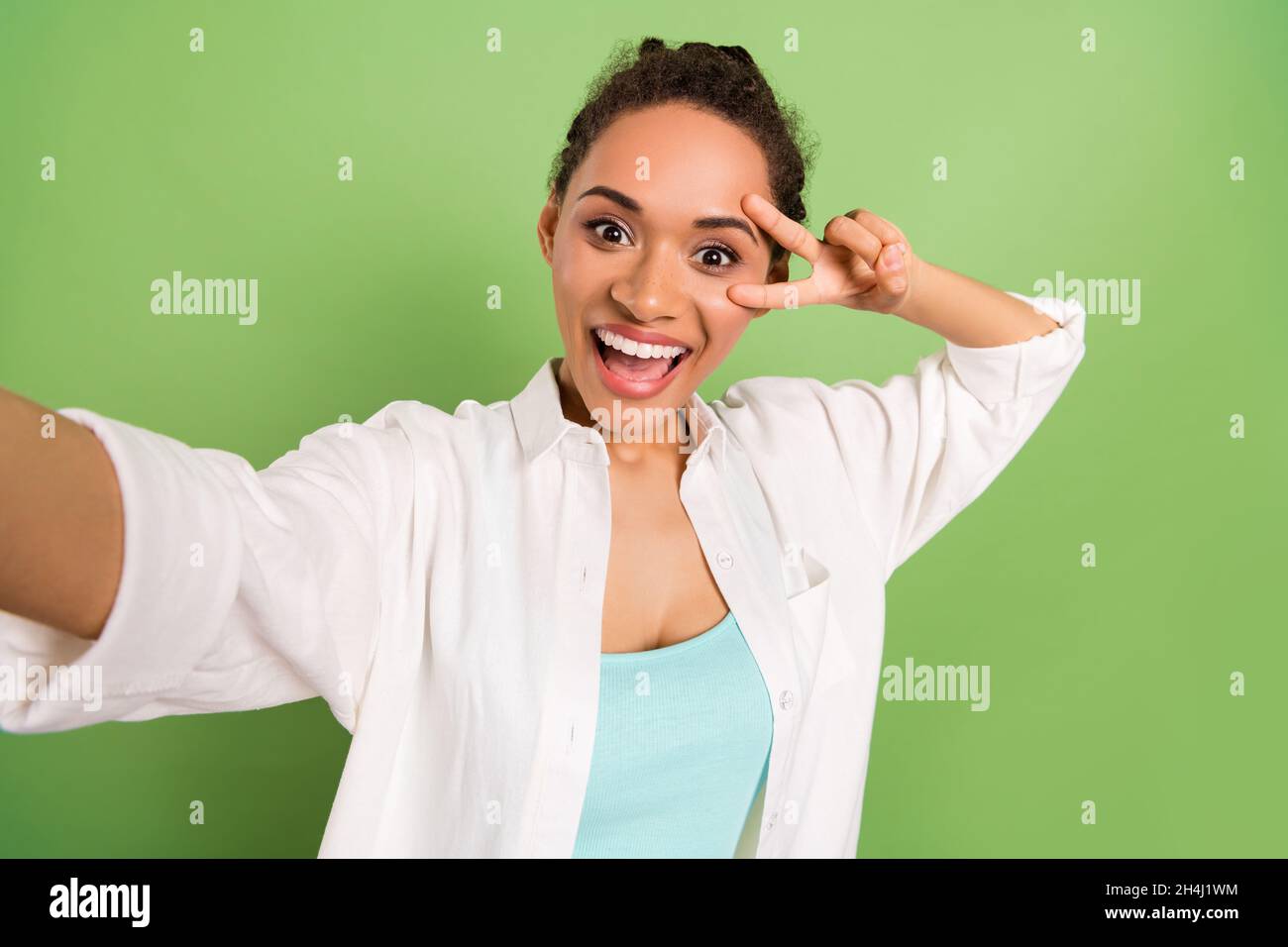 Photo portrait femme avec la coiffure de pain montrant le V-signe prenant selfie isolé surjoyed pastel couleur vert fond Banque D'Images