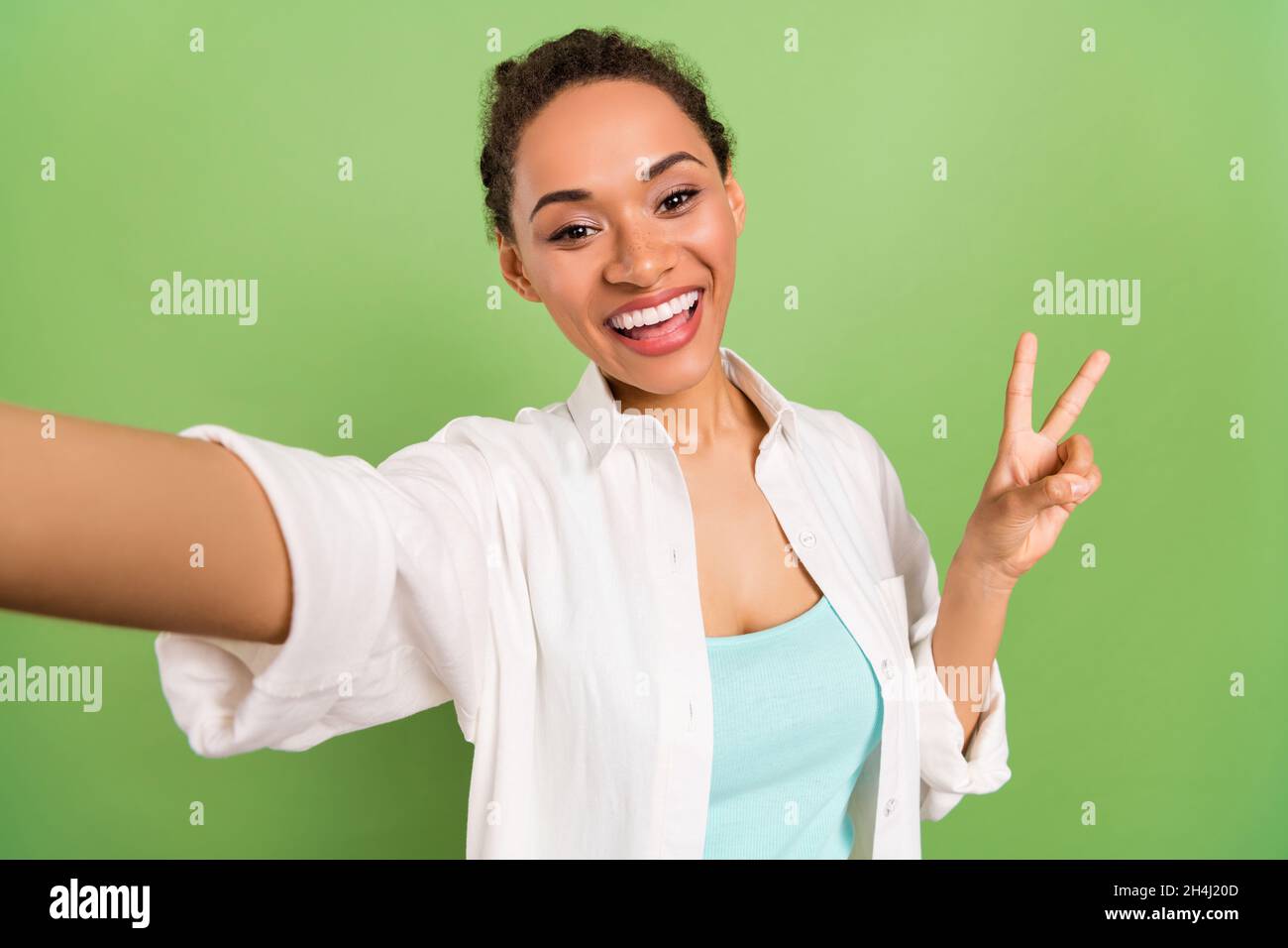 Photo portrait femme avec coiffure de petit pain montrant le V-signe prenant selfie isolé couleur vert pastel arrière-plan Banque D'Images