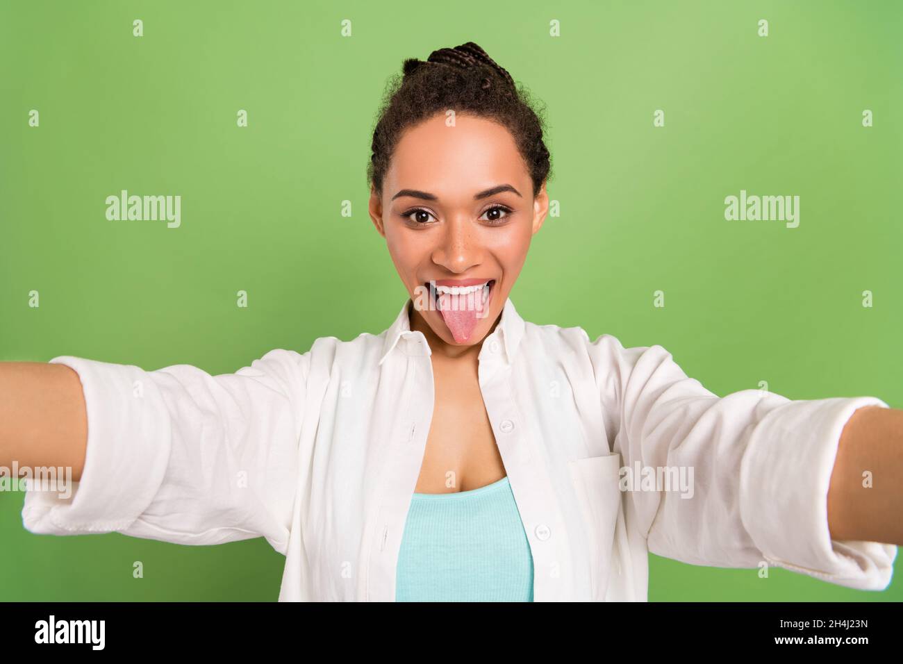 Photo portrait femme avec coiffure de pain montrant la langue prenant selfie isolé couleur vert pastel arrière-plan Banque D'Images