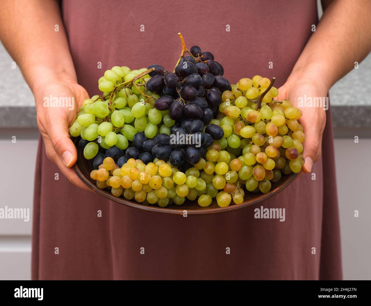 Des grappes de raisin Sultana blanc, bleu et rose sur une assiette dans les mains de la femme. Banque D'Images