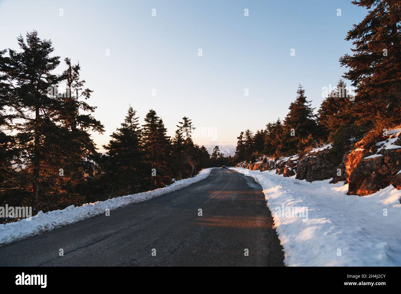 Vider la route asphaltée d'hiver au coucher du soleil au milieu de la zone montagneuse et de la forêt couverte de conifères.Highlands de Grèce, hiver.Liberté, concept de voyage Banque D'Images