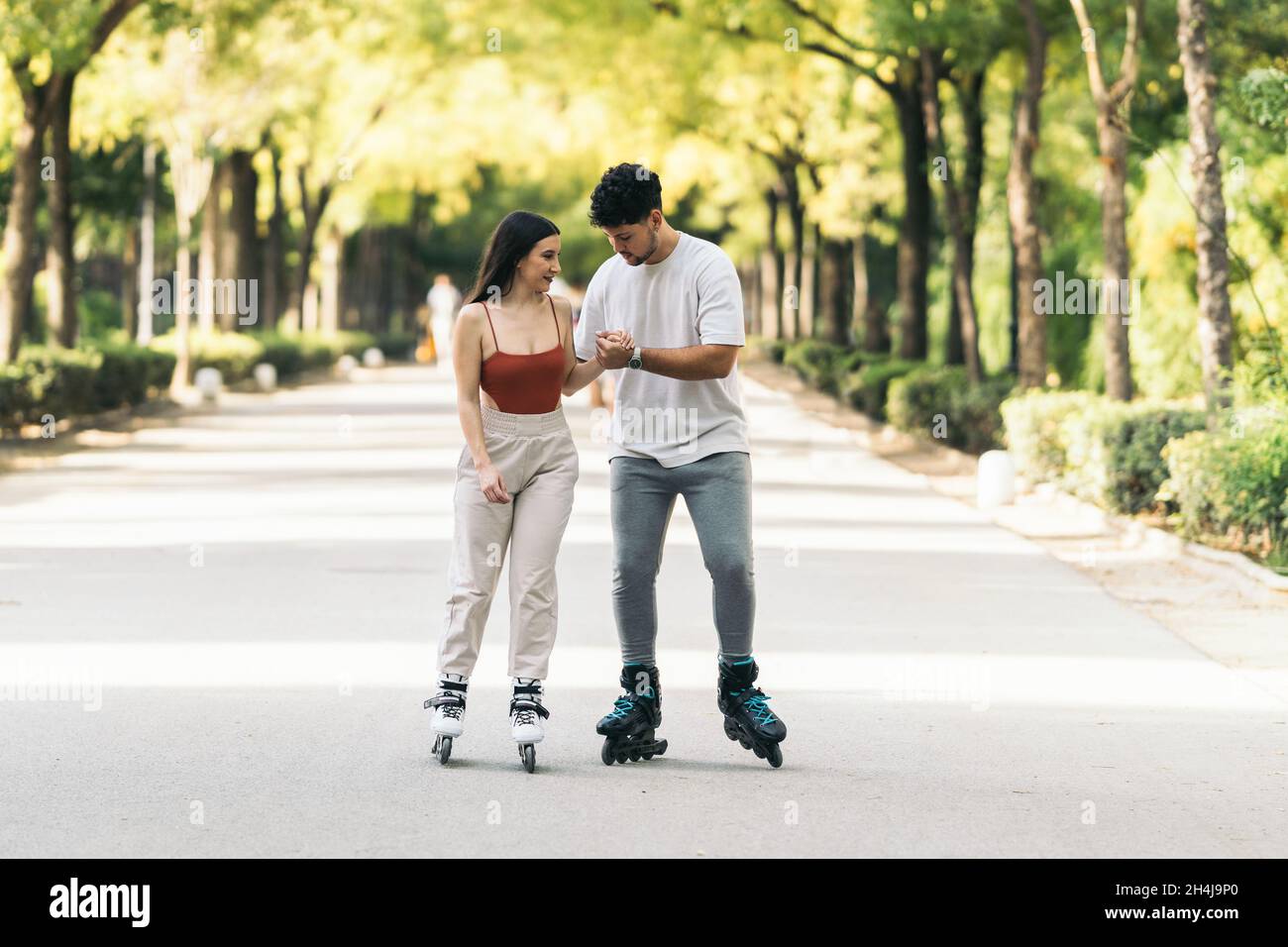 Jeune homme aidant à apprendre à skate à une femme dans un parc public Banque D'Images