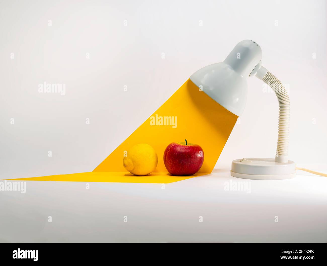 Une pomme et un citron sous un faisceau de lumière conceptuel d'une lampe de table Banque D'Images