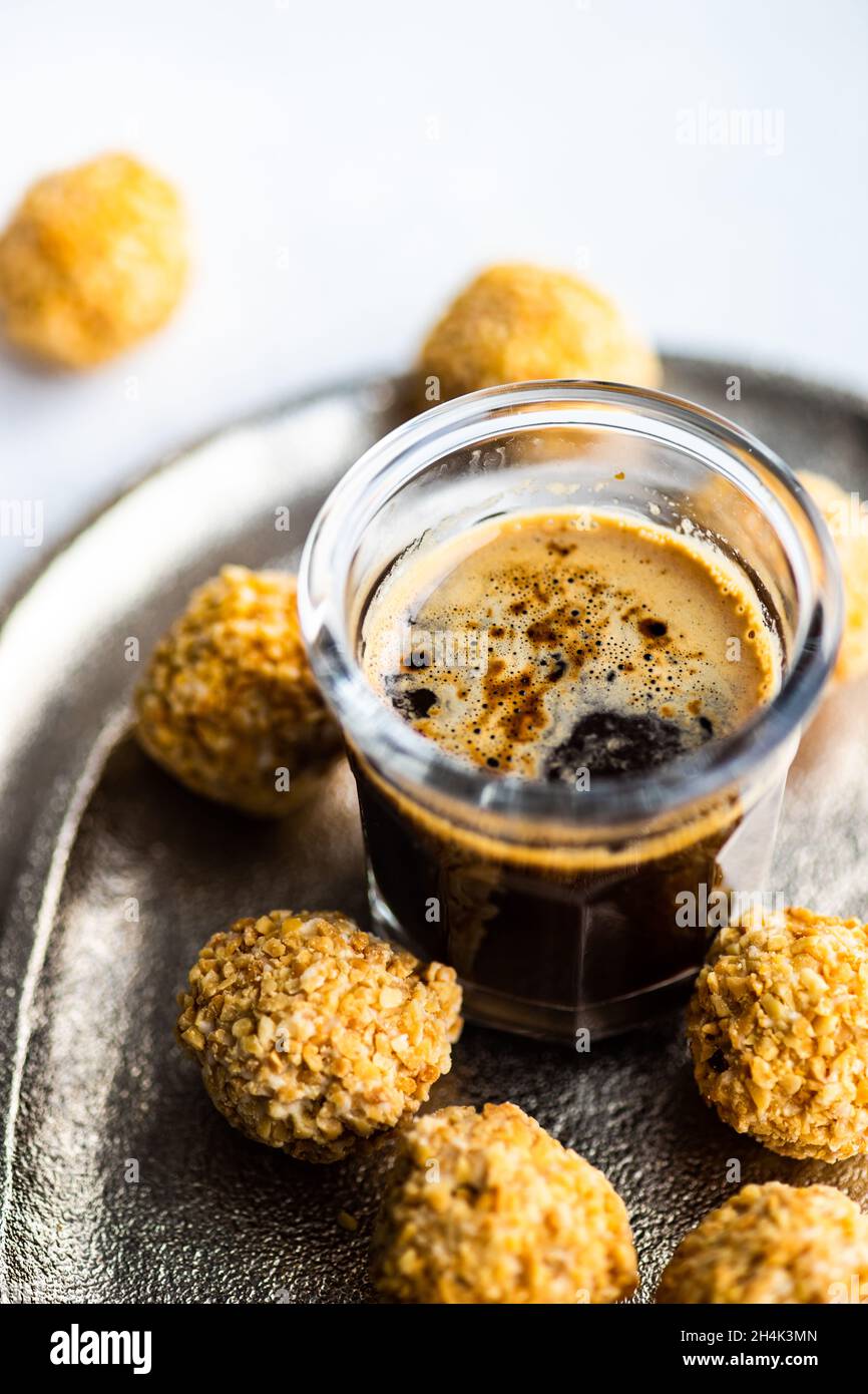Boules de bonbons maison enrobées de noix hachées avec une tasse de café noir Banque D'Images