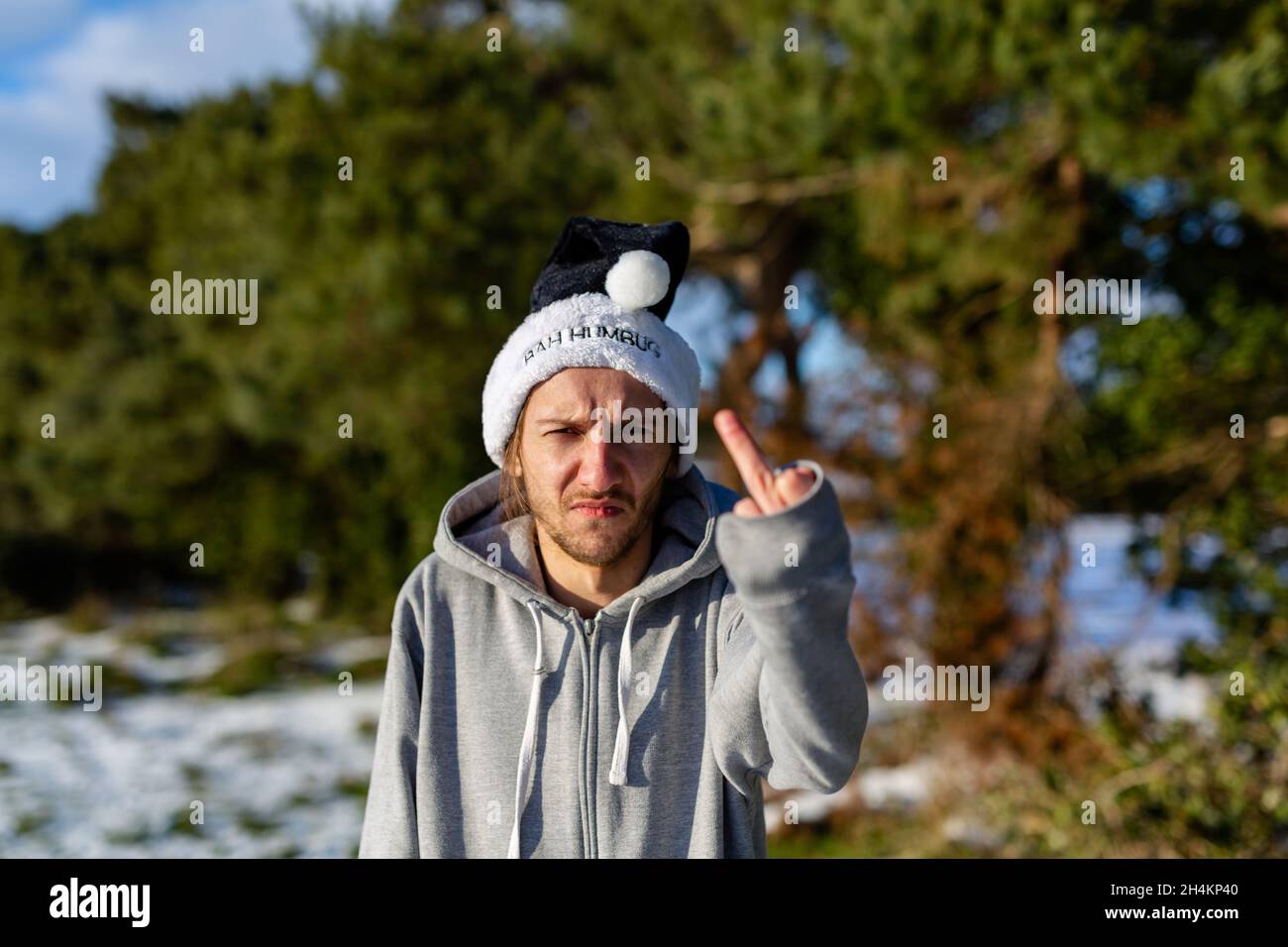 Un jeune homme grincheux portant un chapeau de père noël noir avec les mots Bah Humbug écrits dessus Banque D'Images