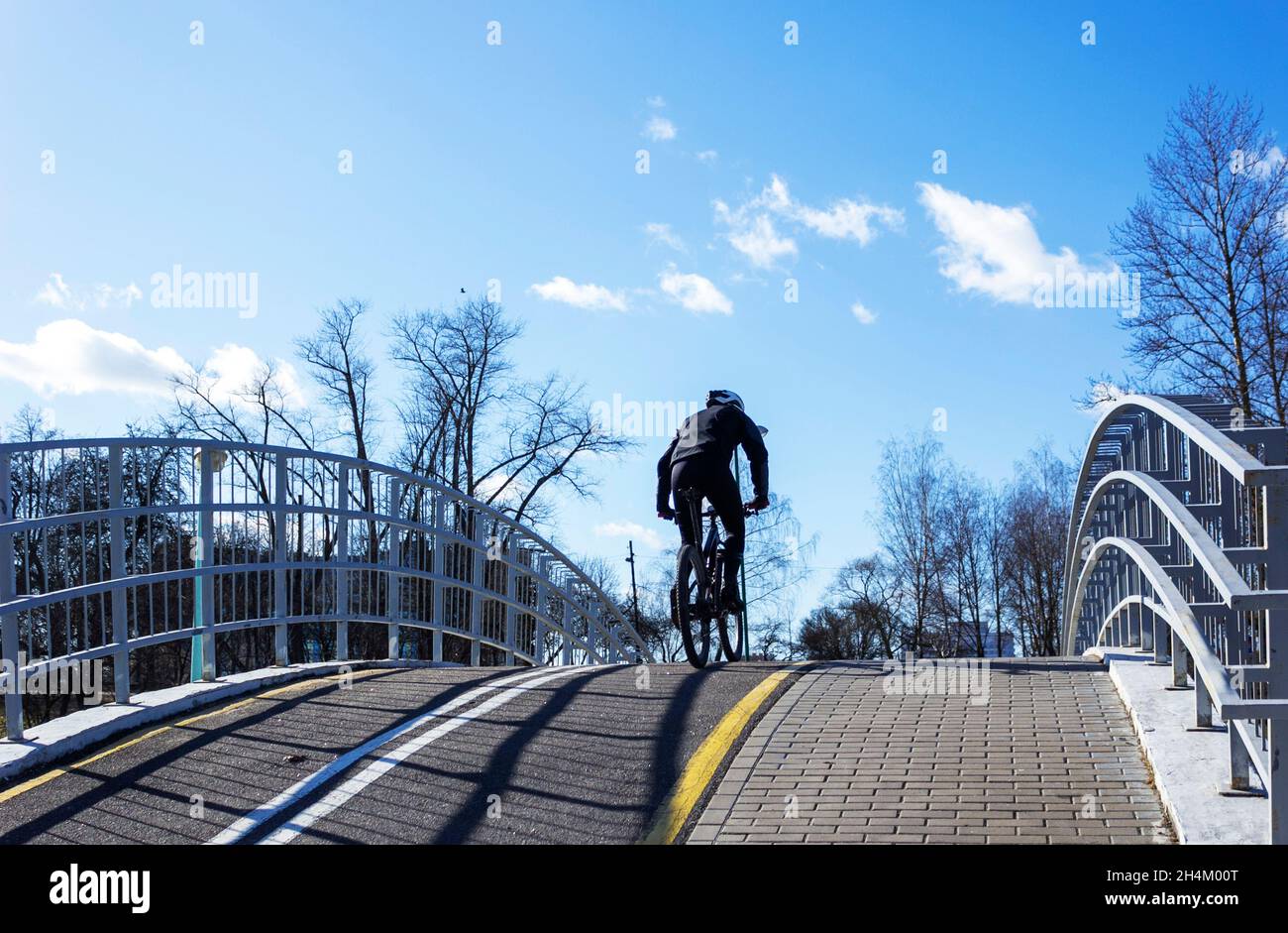 Le jour ensoleillé du printemps, un cycliste monte sur une colline, traverse un pont sur une piste cyclable Banque D'Images