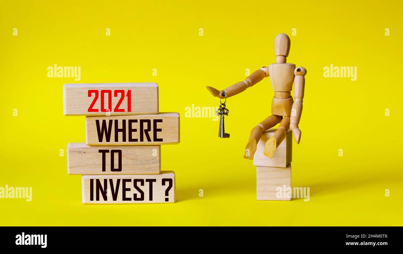 Blocs en bois avec le texte 2021 où investir sur un fond jaune et à côté d'une poupée en bois avec des clés Banque D'Images