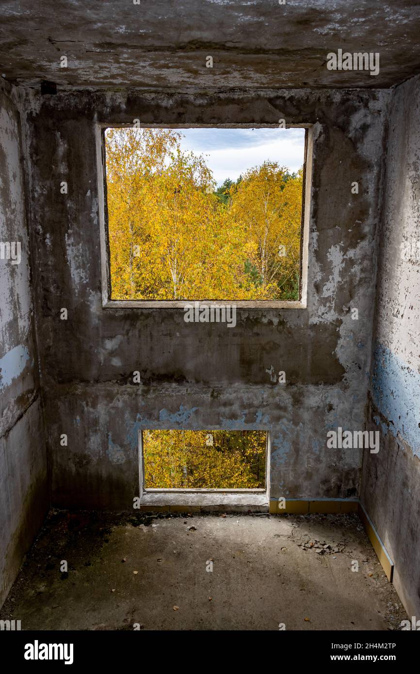 Vue à travers le trou pour une fenêtre dans une maison de panneau abandonnée endommagée. Banque D'Images