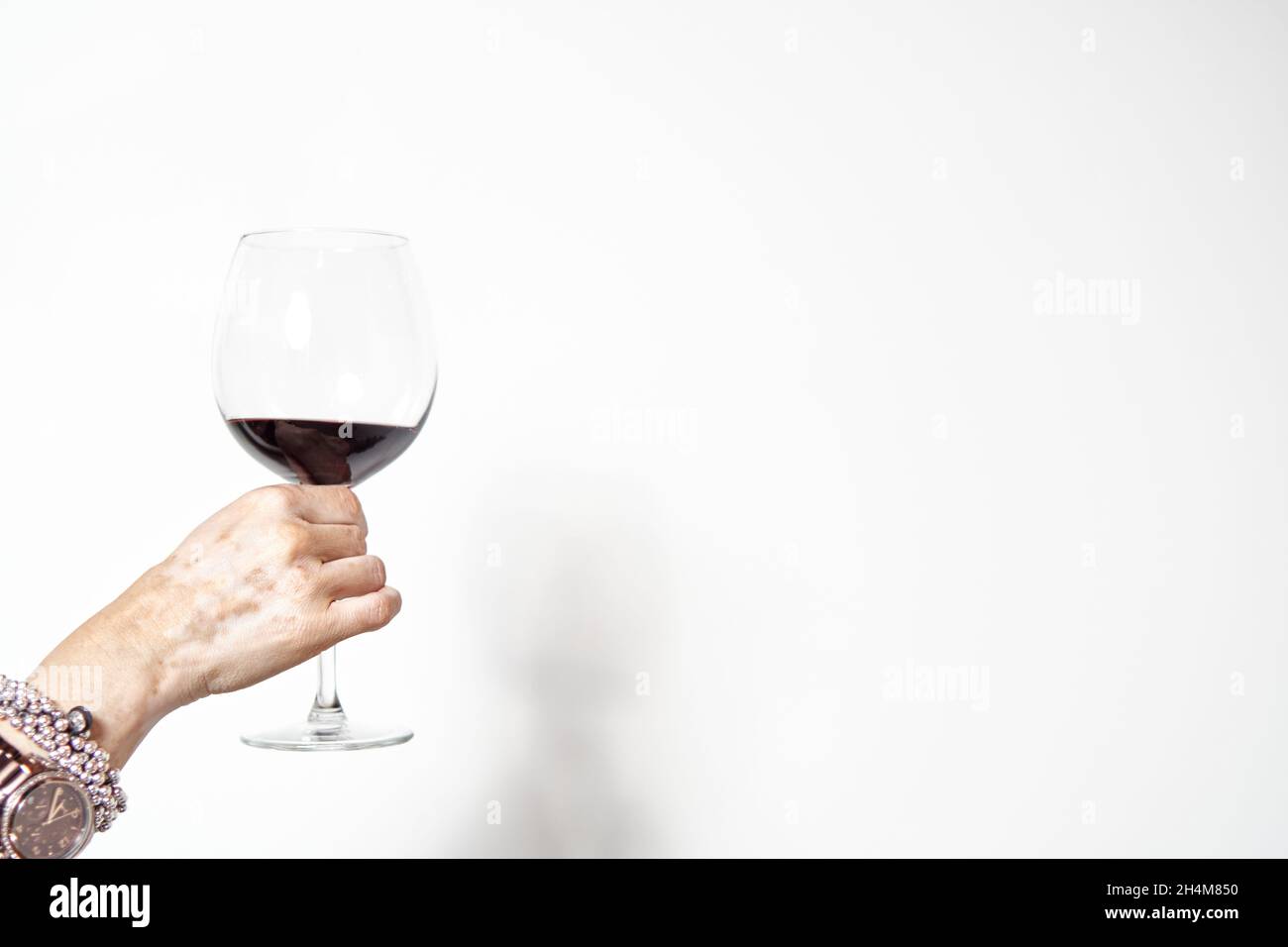 main d'une jeune femme avec le vitiligo toasting avec un verre de vin rouge sur fond blanc. espace copie Banque D'Images