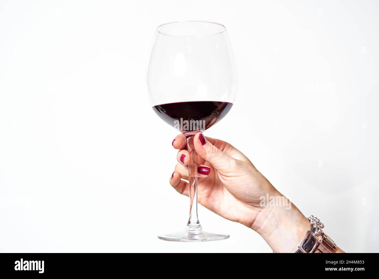 main d'une jeune femme avec du vitiligo et des ongles peints en rouge en brunissage avec un verre de vin rouge sur fond blanc. Banque D'Images