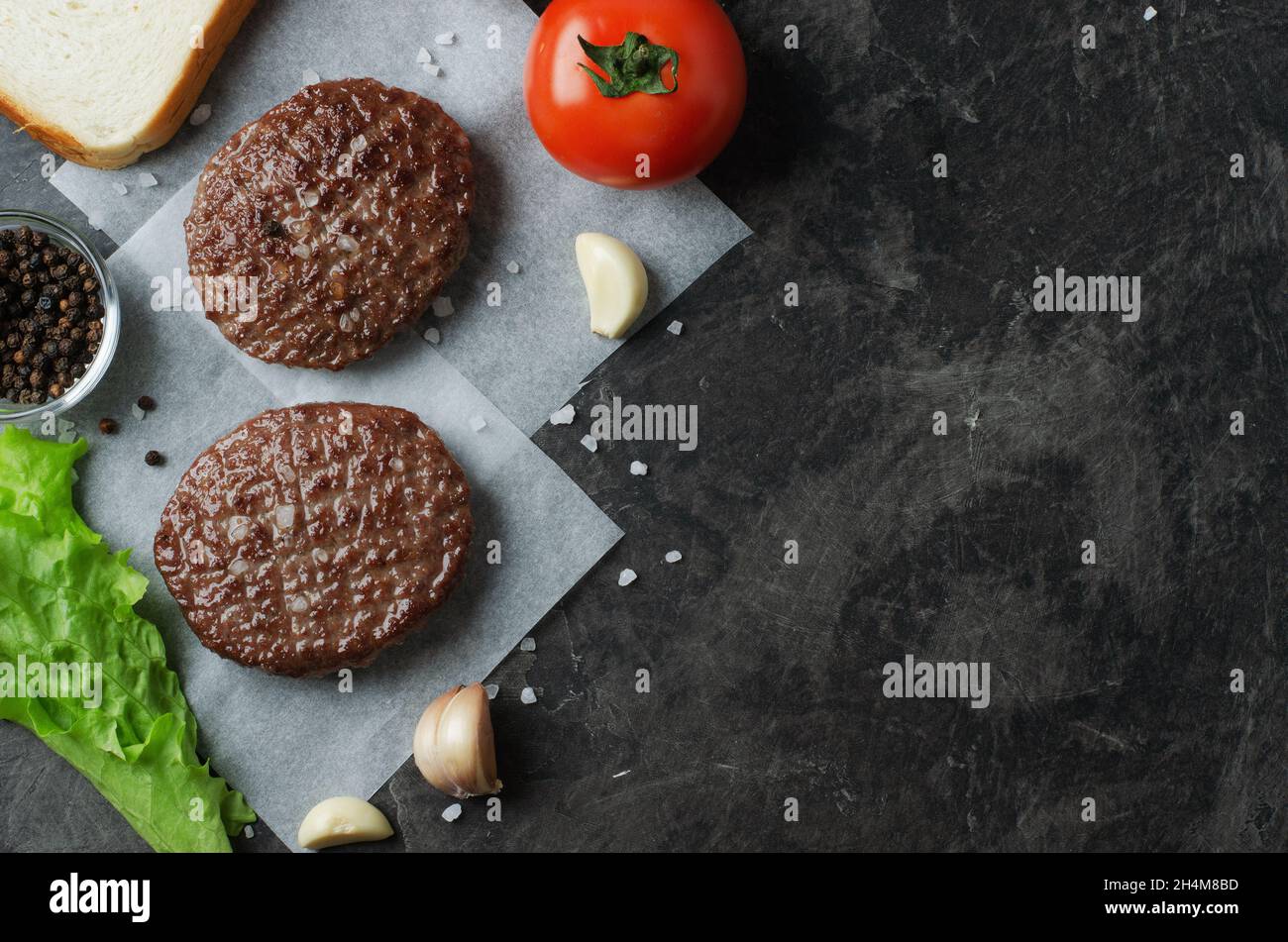 Ingrédient frais frit pour hamburger de bœuf avec tomates, salades et ail sur fond sombre, vue de dessus, espace pour le texte Banque D'Images