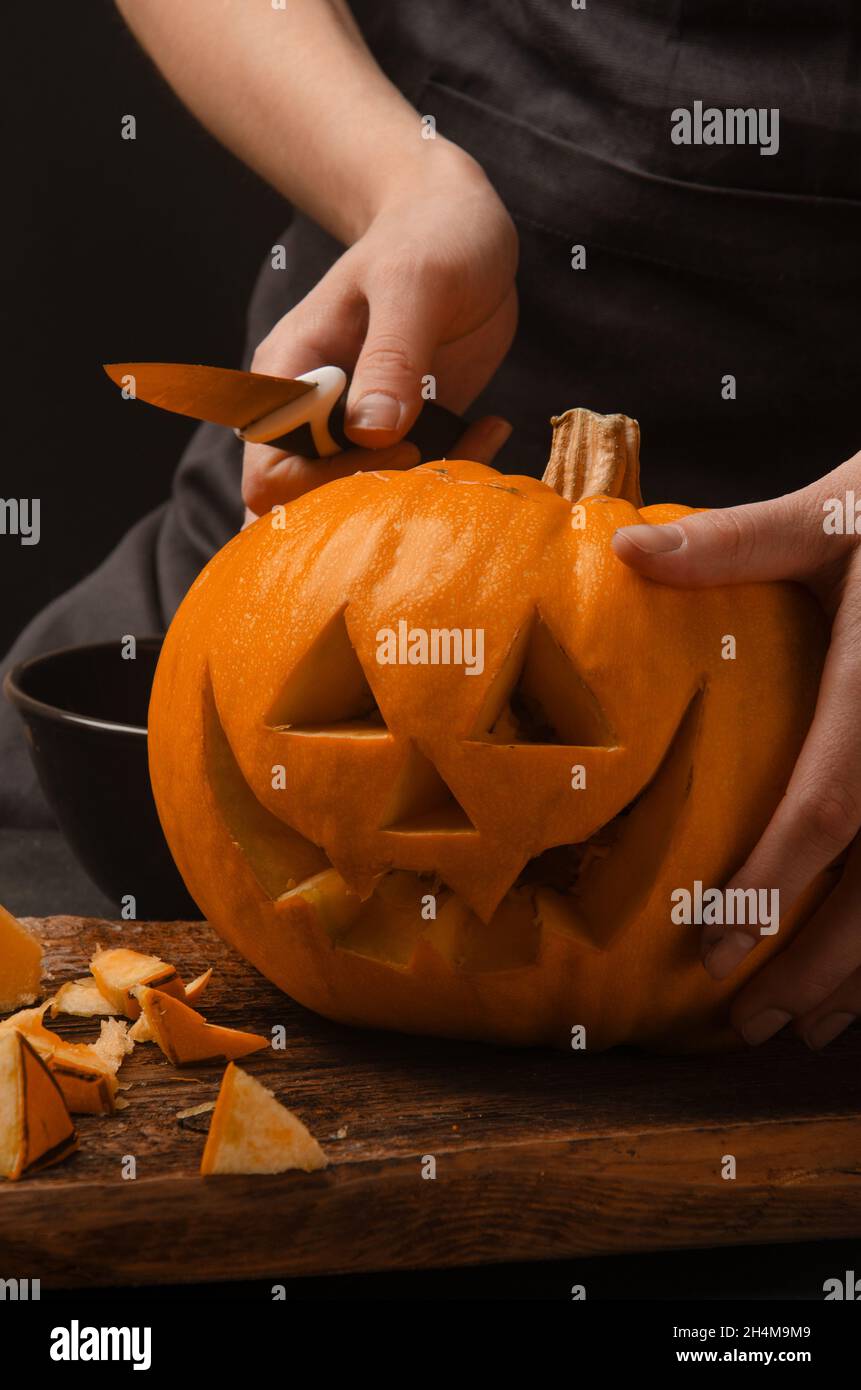 Les mains coupent, sculptant de la citrouille en lanternes de citrouille pour halloween.Sourire halloween citrouille décoration de vacances. Banque D'Images