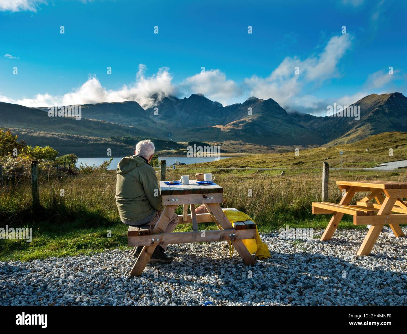 Homme assis dehors à table de pique-nique avec une vue fabuleuse de Blaven dans les montagnes de Cuillin Noire, Amy's place Tearoom, café, Torrin, Skye,Écosse Banque D'Images