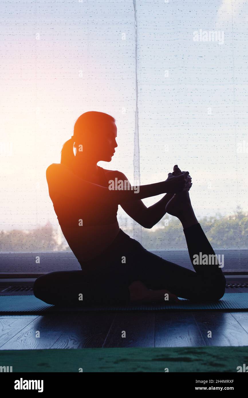 Silhouette de jeune femme faisant du yoga à la maison au coucher du soleil orange Banque D'Images