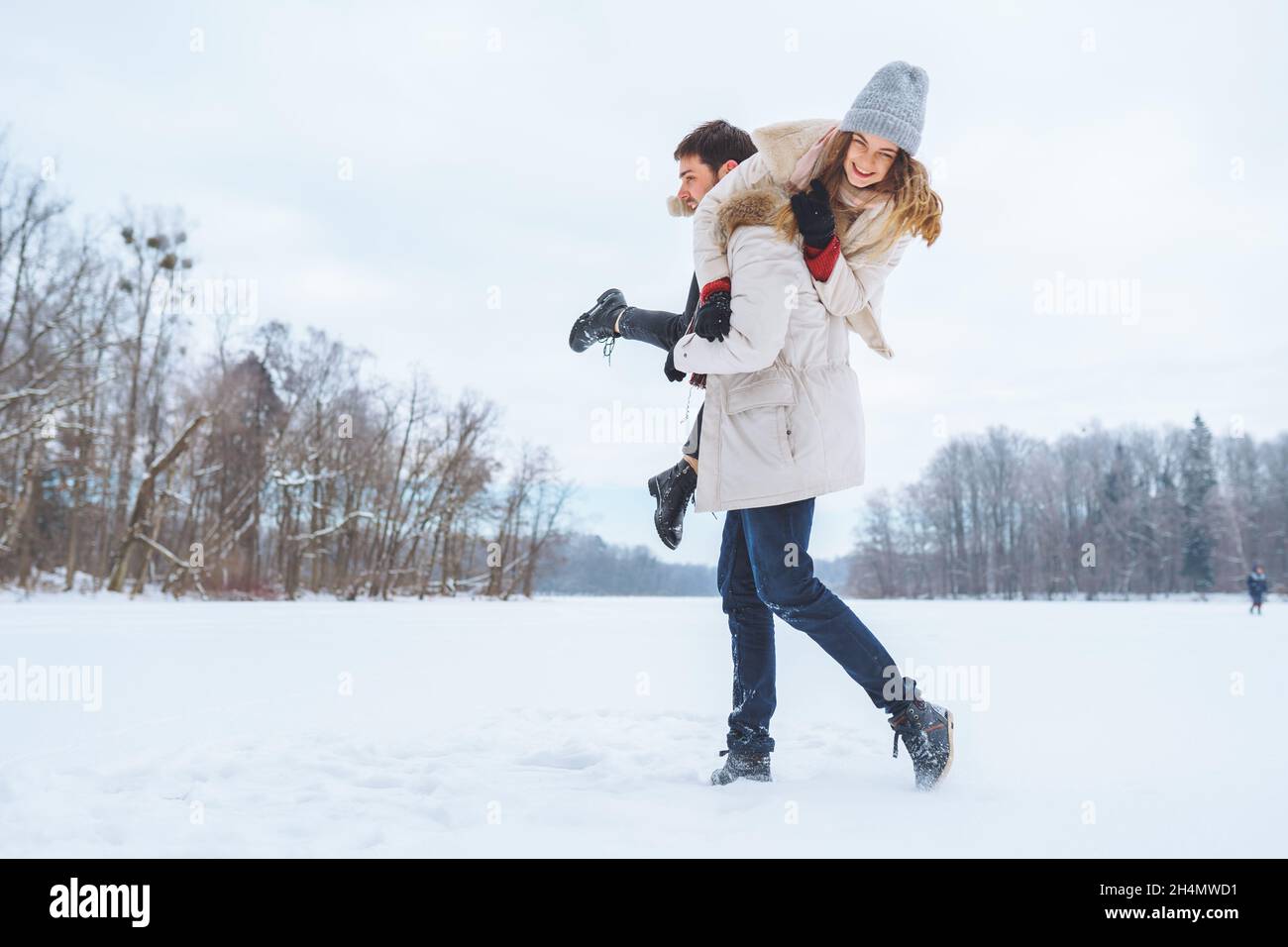 Un jeune homme heureux porte sa jolie femme souriante sur son dos au parc d'hiver. Petit ami donnant le pigegyback sur l'épaule à sa petite amie en hiver Hol Banque D'Images