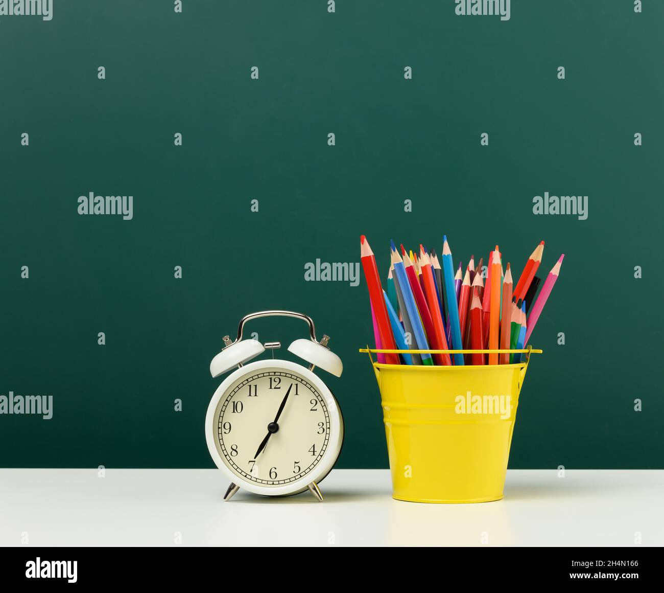 radio-réveil rond et crayons multicolores sur le fond d'un tableau blanc vert vide.Retour à l'école Banque D'Images