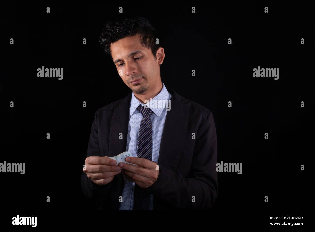 Homme d'affaires comptant de l'argent, isolé sur fond noir.Jeune latin homme portant des vêtements élégants comptant des factures d'argent.Jeune adulte latin jeune homme. Banque D'Images