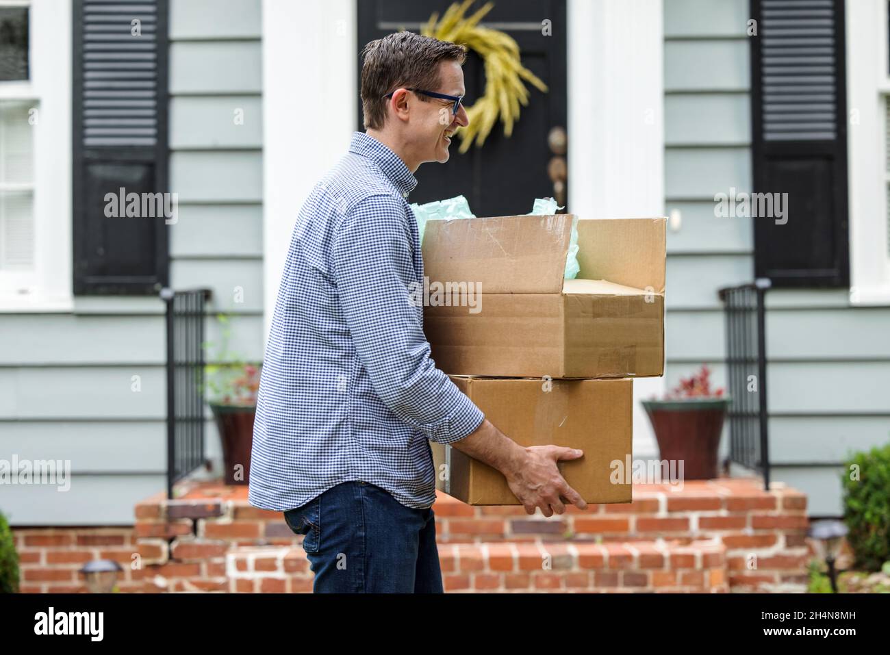 Un homme et un père tenant des boîtes mobiles à l'extérieur d'une petite maison de cottage bleu se préparer à se déplacer dans sa nouvelle maison Banque D'Images