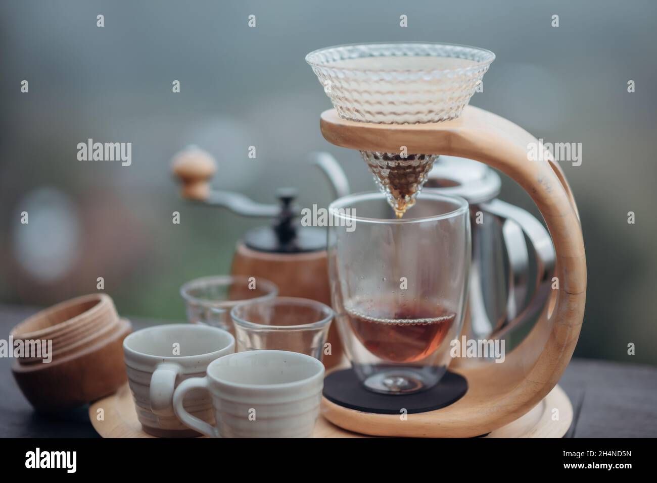 Un nécessaire à café goutte-à-goutte avec une bouilloire en acier, un verre et une cafetière goutte-à-goutte dans un style minimaliste avec un fond de brouillard et de nature. Banque D'Images Un nécessaire à café goutte-à-goutte avec une bouilloire en acier, un verre et une cafetière goutte-à-goutte dans un style minimaliste avec un fond de brouillard et de nature. Banque D'Images